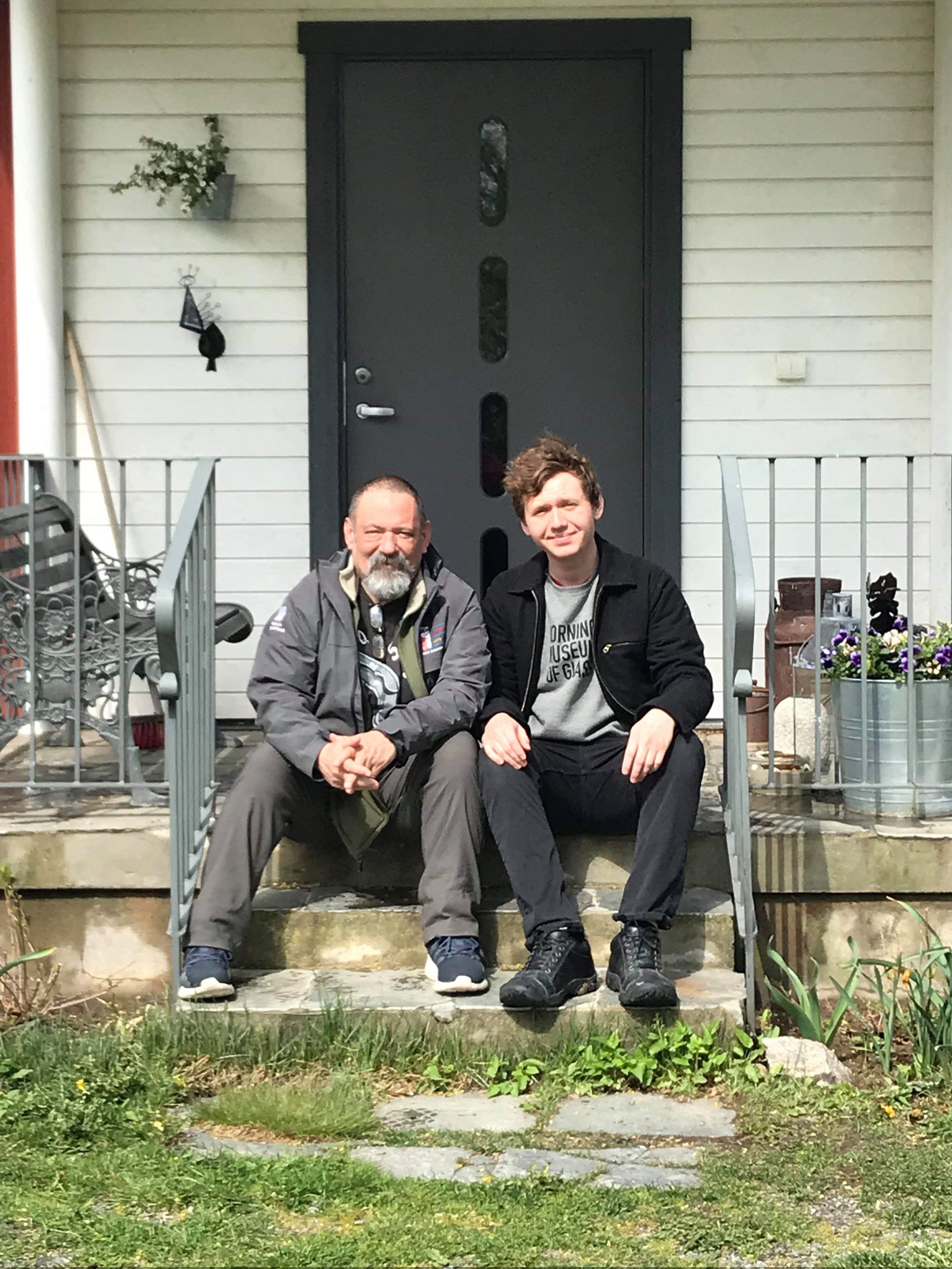 Caleb Carlson and his father, glass artist Kurt Carlson, sitting together on outdoor steps